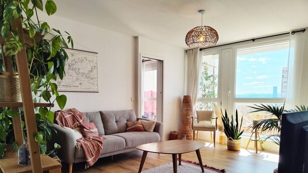 A living room with a sofa, coffee table, and plants. There is a map on the wall and a window with curtains.