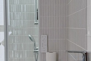 Une salle de bain équipée d’une douche, d’un porte-rouleau de papier toilette et d’un panneau de commande.