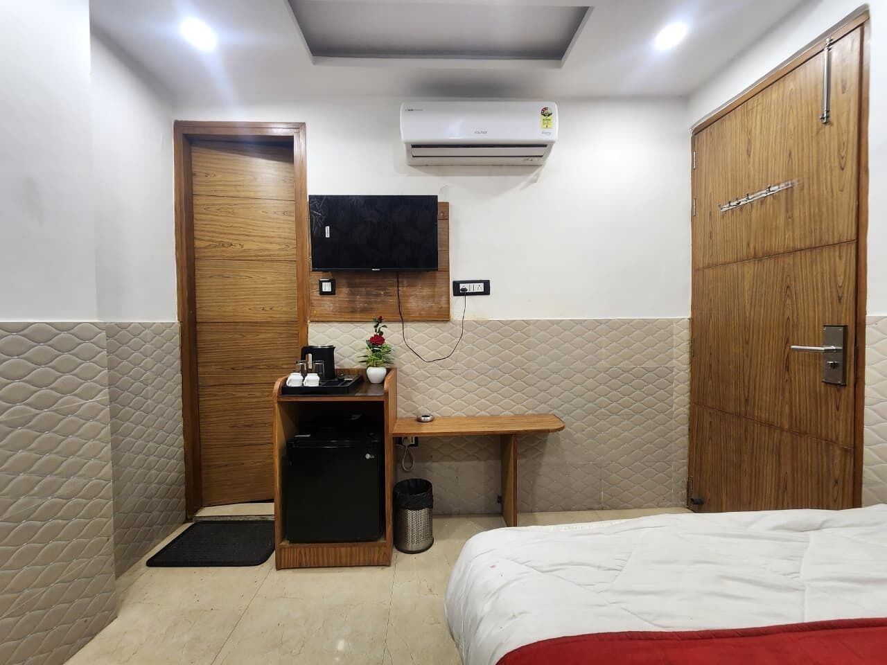 A hotel room with a bed, a desk, a television, and an air conditioning unit.