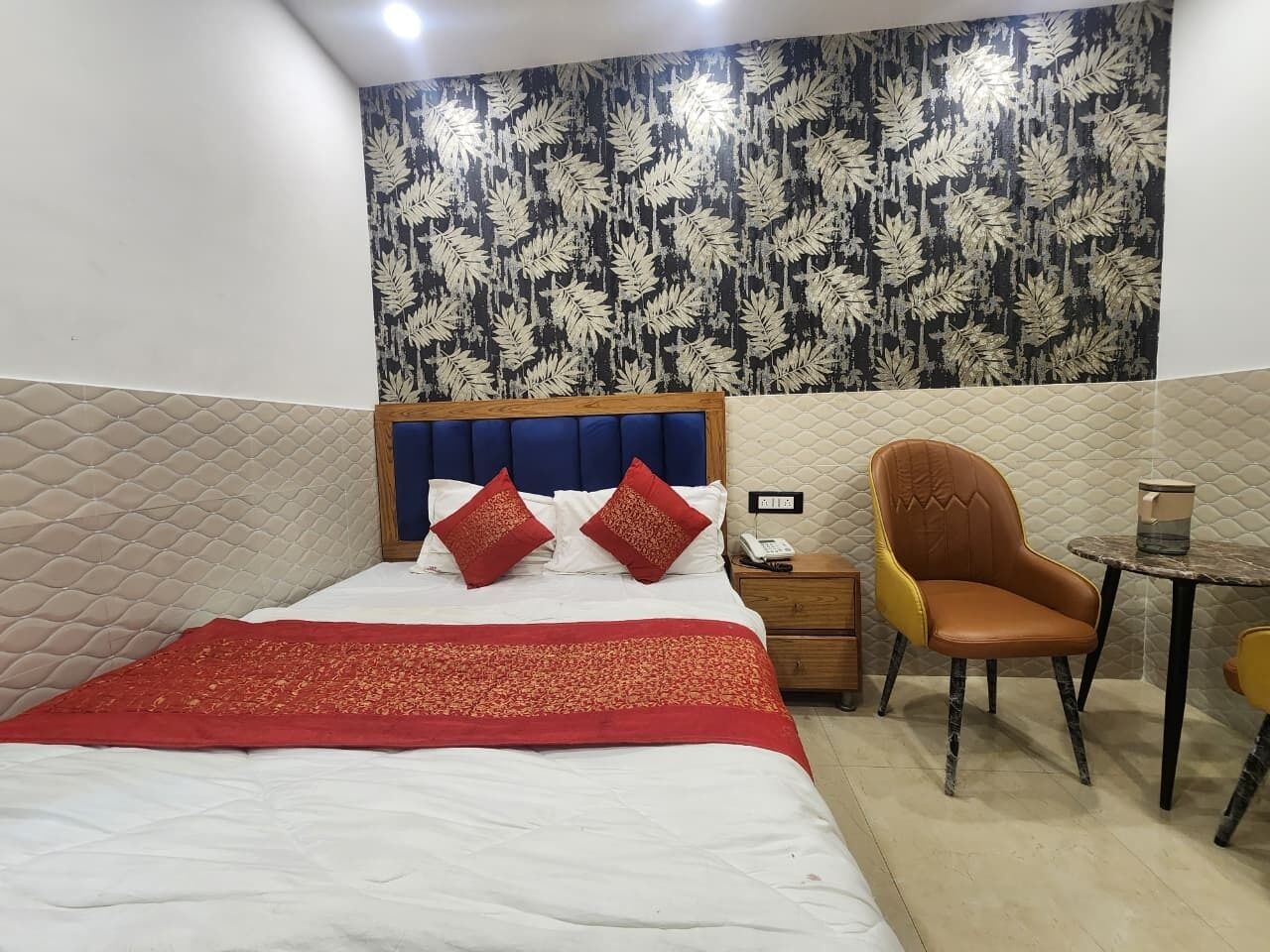 A hotel room with a bed, a bedside table with a phone, a chair, and a small round table.