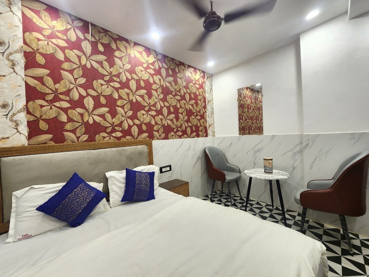 A hotel room with a bed, two chairs, a small table, and a ceiling fan.