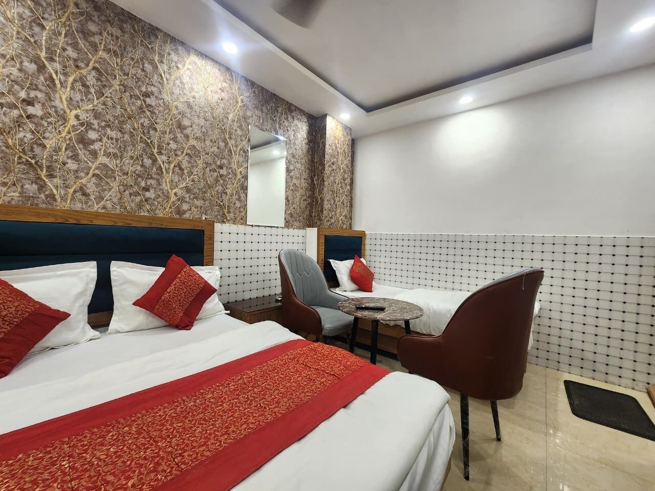 A hotel room with two beds, a sitting area with a table and chairs, a large mirror, and a patterned wall.