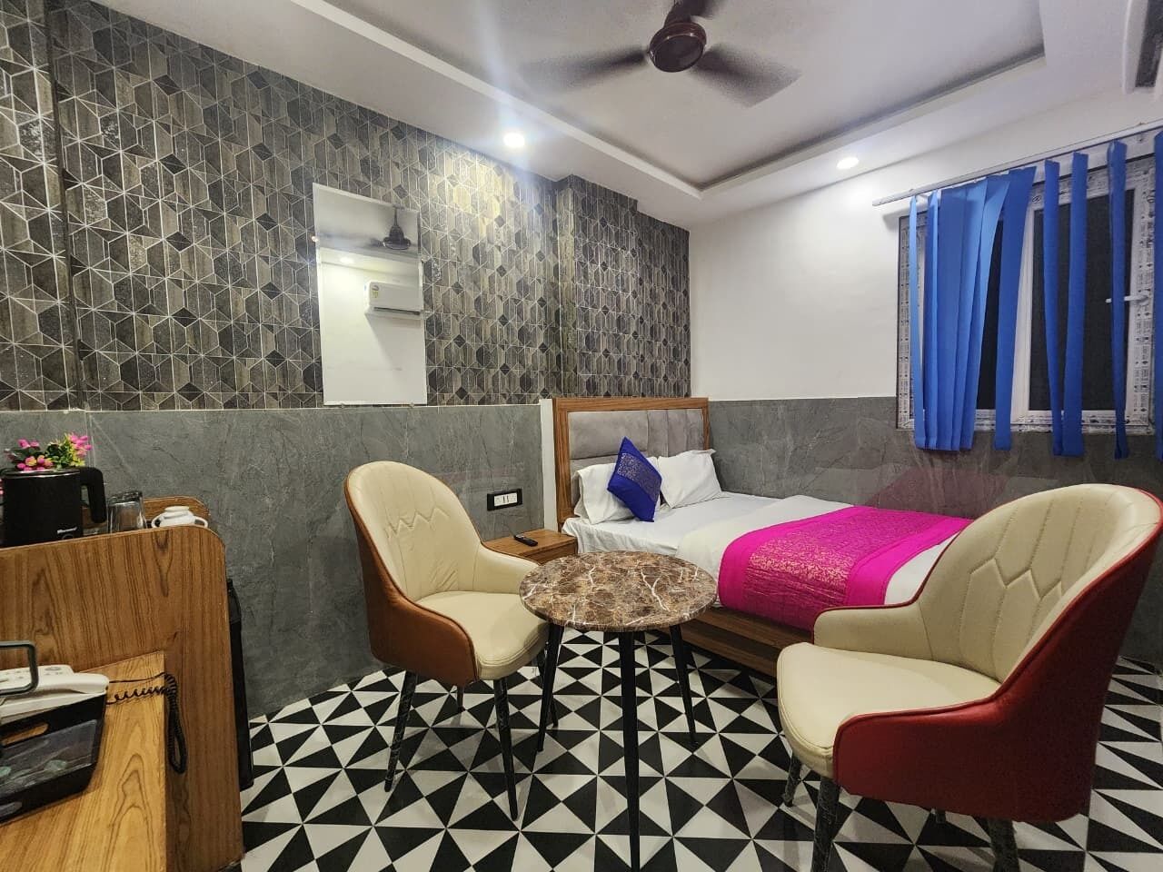 Una habitación de hotel con una cama, dos sillones, una mesita redonda, un escritorio de madera y un suelo con estampado.