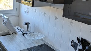 Una cocina moderna con una placa de inducción negra, electrodomésticos de acero inoxidable y un ventanal con vistas a árboles.