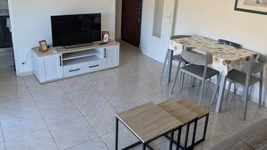 Una sala de estar con televisor, sofá, mesa de comedor y sillas.