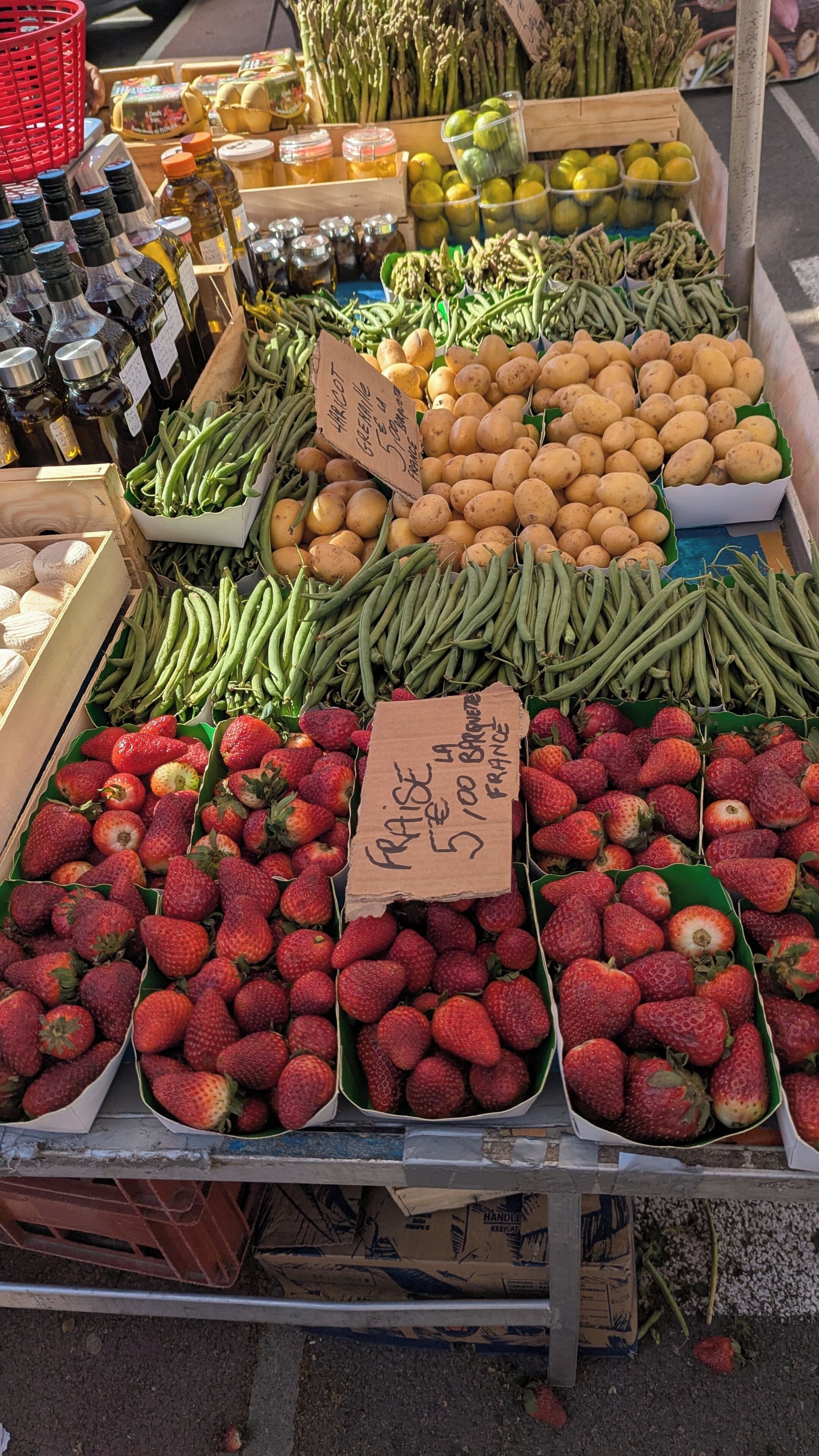 A market stall with various fresh produce including strawberries, potatoes, and green beans.