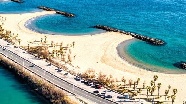 Vista aérea de una zona costera con playa, aguas azules cristalinas y una carretera que bordea la orilla.