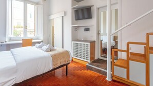 A hotel room with a bed, a desk, a TV mounted on the wall, and a staircase. - Dea Roma (Rome)