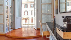 A modern kitchen with a built-in espresso machine, wooden flooring, and a view of the street through large windows. - Dea Roma (Rome)
