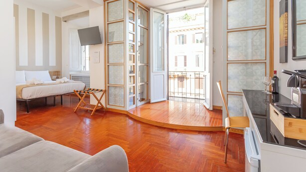 A modern living room with a wooden floor, a sofa, a dining area with a table and chairs, and a kitchen with a coffee machine. - Dea Roma (Rome)