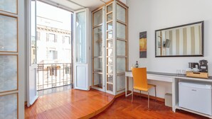A modern room with a wooden floor, a desk, a chair, a small fridge, and a large mirror. - Dea Roma (Rome)