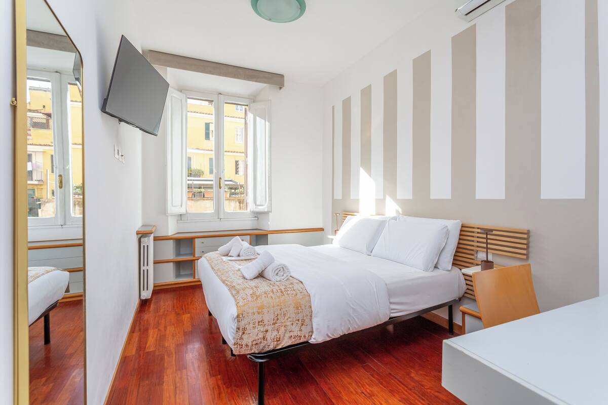 A modern hotel room with a bed, bedside table, chair, and a TV mounted on the wall.