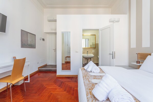 A hotel room with a bed, a desk, a chair, a mirror, and a bathroom visible through an open door. - Dea Roma (Rome)