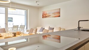 Ett modernt kök med en central köksö, en matplats med stolar och ett bord samt ett stort fönster som släpper in naturligt ljus.