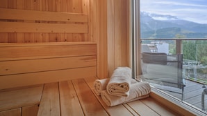 A wooden sauna with a bench and a view of mountains through a large window. - Penthouse Cassiopeia (Tauplitz)