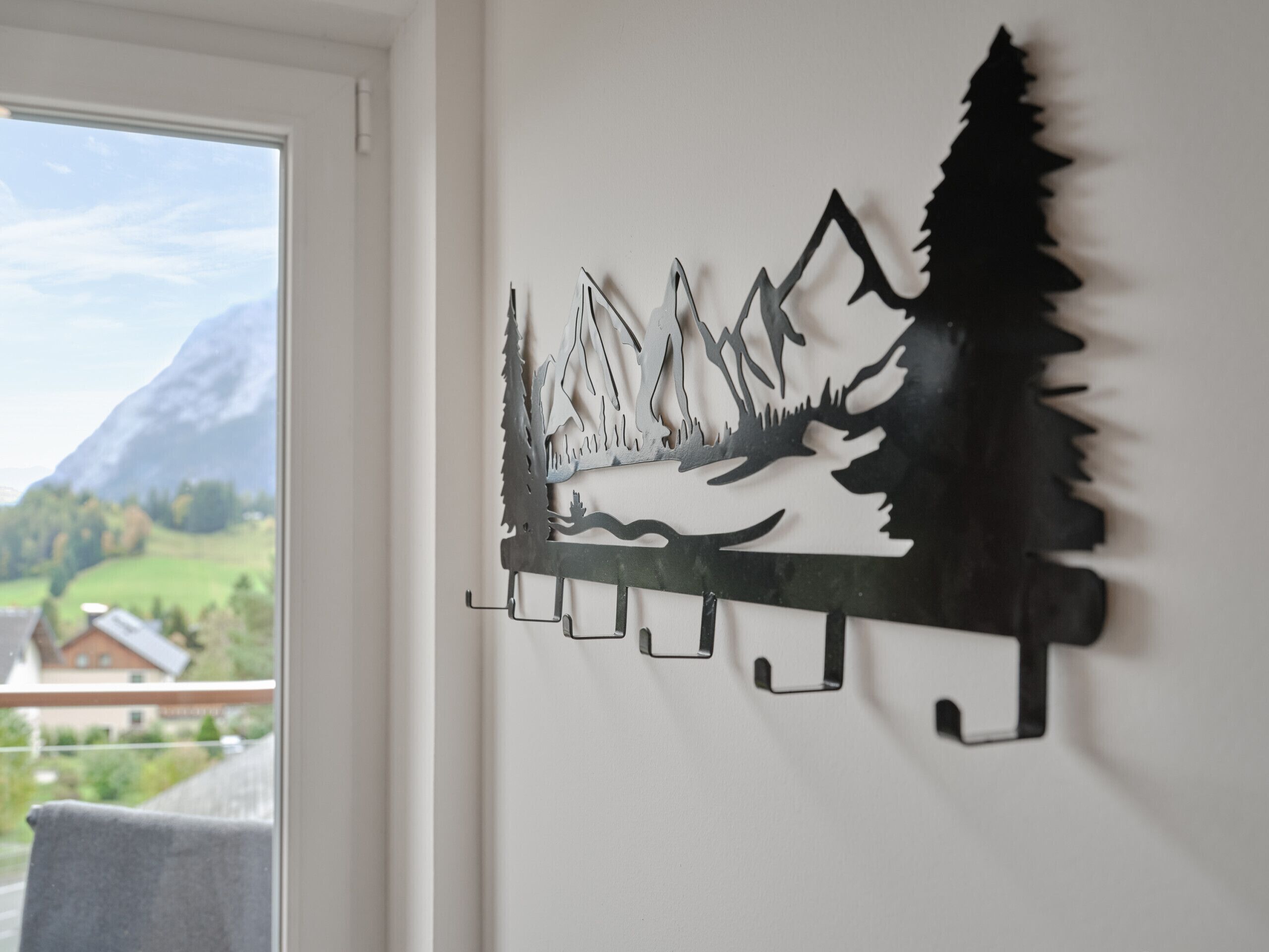 A wall-mounted metal artwork depicting a mountain landscape with trees and a cabin.