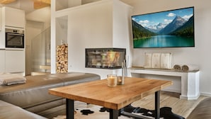 A modern living room with a wooden ceiling, a flat-screen TV mounted on the wall, a wooden coffee table, a leather sofa, and a fireplace. - Penthouse Cassiopeia (Tauplitz)