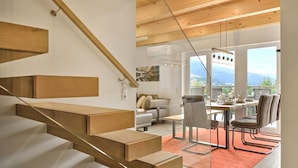 A modern interior with a wooden staircase, a dining area with a view, and a cozy seating area. - Penthouse Cassiopeia (Tauplitz)