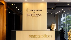 A reception desk with a wooden finish and a Buddha statue on top. The wall above the desk displays the text "WINTER LINE INN By: LUSH LUXE HOSPITALITY". - Hotel Winter Line Inn Near St Francis Monastery (Mussoorie)