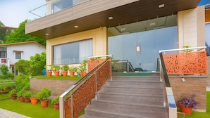 A modern building with a glass entrance, a staircase with metal railings, and potted plants around the entrance area. - Hotel Winter Line Inn Near St Francis Monastery (Mussoorie)
