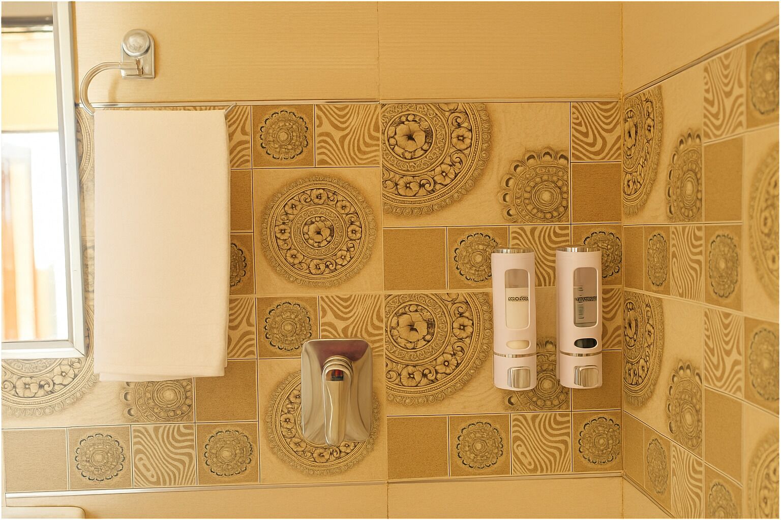 A bathroom with patterned tiles, a towel rack, and two hand dryers.