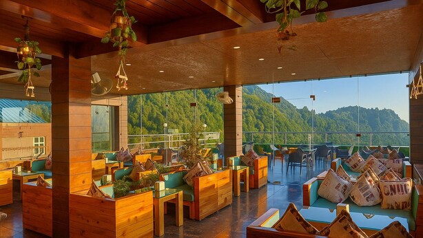 A spacious indoor area with wooden furniture, large windows offering a view of a forested mountain, and hanging light fixtures. - Hotel Winter Line Inn Near St Francis Monastery (Mussoorie)