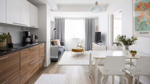 A modern kitchen with wooden cabinets, a black countertop, and a dining area with white chairs and a table. - New Stylish 1BR Apt. in Trendy Kallio (Helsinki)