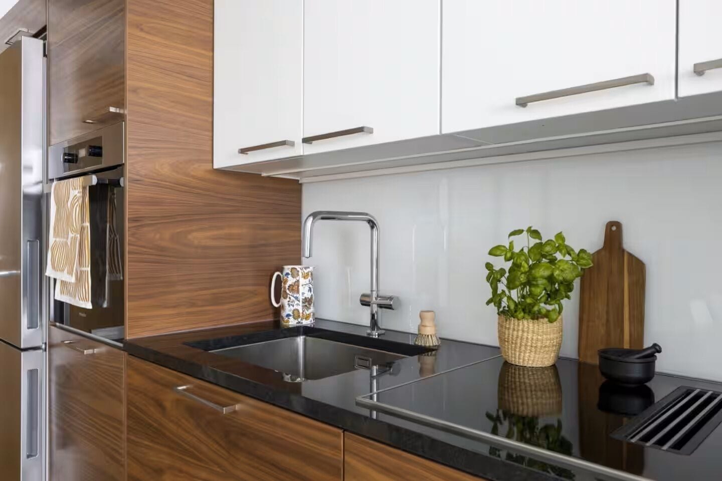Eine moderne Küche mit Holzausstattung, einer Spüle aus Edelstahl und einer schwarzen Arbeitsplatte.