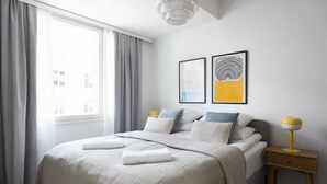 A modern bedroom with a large bed, grey curtains, and two wall art pieces. - New Stylish 1BR Apt. in Trendy Kallio (Helsinki)