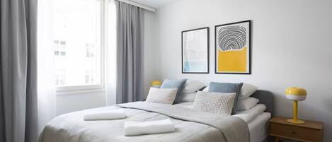 Una camera da letto moderna con un letto grande, tende grigie e due opere d'arte a parete.