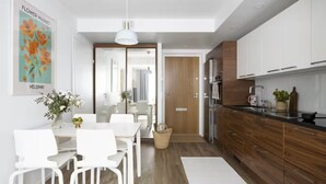 A modern kitchen with wooden cabinets, a black countertop, and stainless steel appliances. There is a dining area with white chairs and a table, and a large window providing natural light. - New Stylish 1BR Apt. in Trendy Kallio (Helsinki)