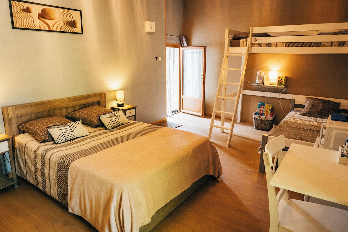 Una habitació amb un llit gran, un llit superposat, un escriptori i una escala.