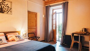 A bedroom with a bed, a wooden table, a chair, and a window with curtains. - Domaine de cozance (Anjou)