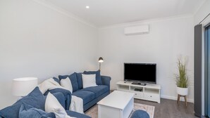 A modern living room with a blue sofa, white coffee table, and a flat-screen TV on a white stand.