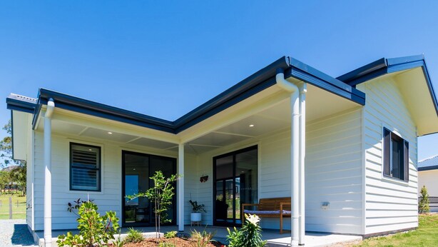A modern house with a covered porch, large windows, and a small garden area.