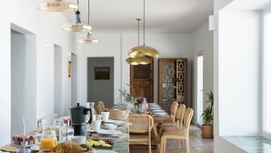 A dining area with a long table set for a meal, surrounded by wicker chairs, and a coffee station with a coffee maker and cups.