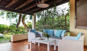 Un patio al aire libre con mobiliario de mimbre, una lámpara colgante y vistas a la vegetación.