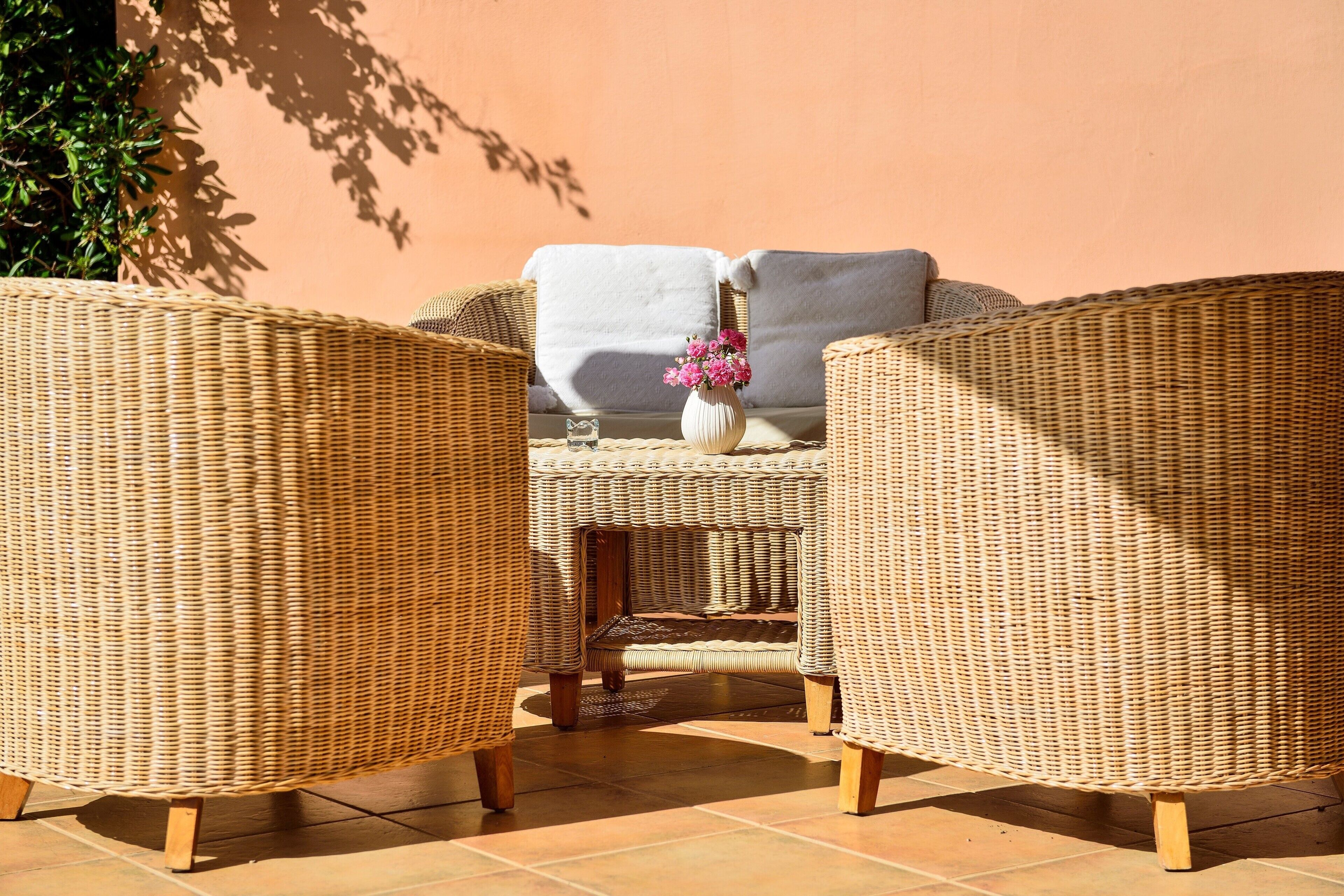 Wicker furniture, a white cushion, and a vase with pink flowers on a patio.