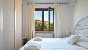 A neatly made bed with white linens and towels, a white headboard, and a window with curtains.