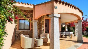 A covered patio area with wicker furniture, stone pillars, and a view of the garden.