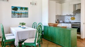 A kitchen with white cabinets, a green island, and a dining area with green chairs and a white tablecloth.