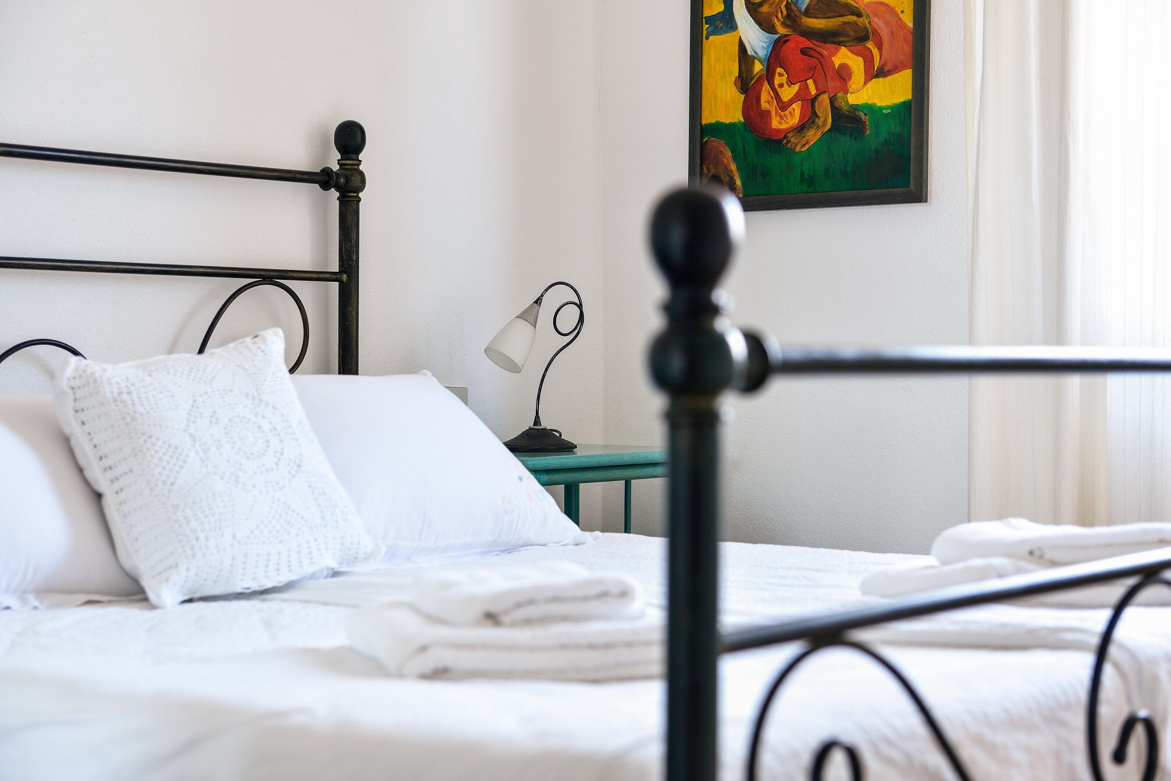 Una cama bien tendida con sábanas blancas, un cabecero de metal negro y una mesita de noche con una lámpara.