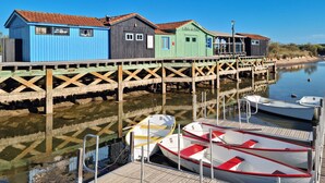 Une rangée de bâtiments en bois aux couleurs vives, avec une jetée qui s’avance dans une étendue d’eau calme, où des bateaux sont amarrés.