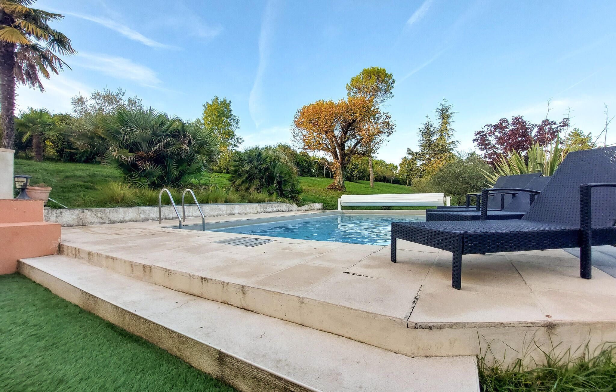 A swimming pool with a small deck area, surrounded by lush greenery and trees.