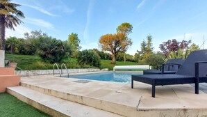 Une piscine avec un petit espace aménagé autour, entourée d’une végétation luxuriante et d’arbres.