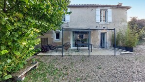 Une maison à deux étages dotée d’un patio couvert, d’un petit jardin et d’une allée en gravier.