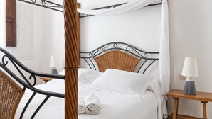 A bed with a wicker headboard, white bedding, and a rolled towel. - Villa Fiori 4 Is Molas – Exclusive Villa with Private Pool and Sea View in Sardinia (S.Margh.di Pula)