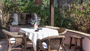 An outdoor patio with wicker furniture, a table with a white tablecloth, a grill, and a hanging light fixture. - Villa Fiori 4 Is Molas – Exclusive Villa with Private Pool and Sea View in Sardinia (S.Margh.di Pula)