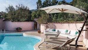 A swimming pool with a curved edge, a lounge area with chairs and a sofa, and a large umbrella providing shade. - Villa Fiori 4 Is Molas – Exclusive Villa with Private Pool and Sea View in Sardinia (S.Margh.di Pula)