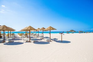 A beach with sun loungers and thatched umbrellas. - Villa Fiori 4 Is Molas – Exclusive Villa with Private Pool and Sea View in Sardinia (S.Margh.di Pula)